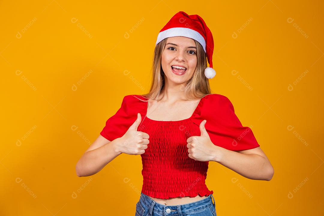 Mulher loira bonita positiva com chapéu de Papai Noel e roupa vermelha para o natal. Jovem mulher vestida para o Natal sorrindo.