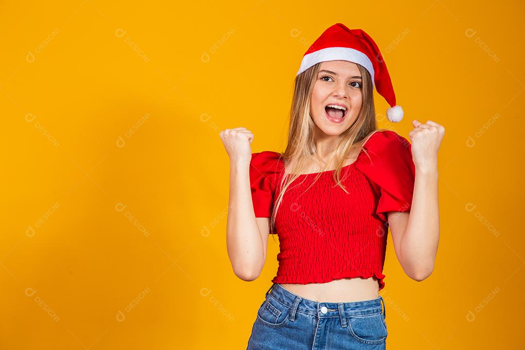 Mulher com roupa vermelha e gorro de natal com expressão de felicidade em fundo amarelo