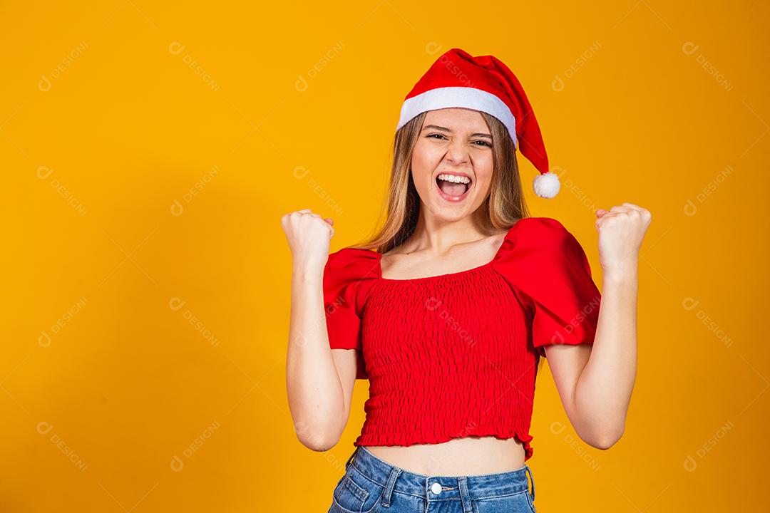 Mulher com roupa vermelha e gorro de natal com expressão de felicidade em fundo amarelo