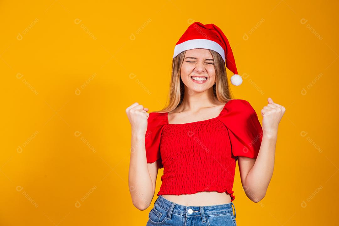 Mulher com roupa vermelha e gorro de natal com expressão de felicidade em fundo amarelo