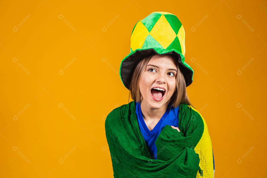 fã brasileira loira comemorando em fundo amarelo com bandeira do brasil