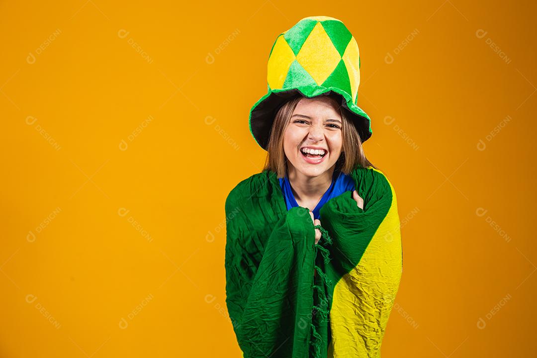 fã brasileira loira comemorando em fundo amarelo com bandeira do brasil