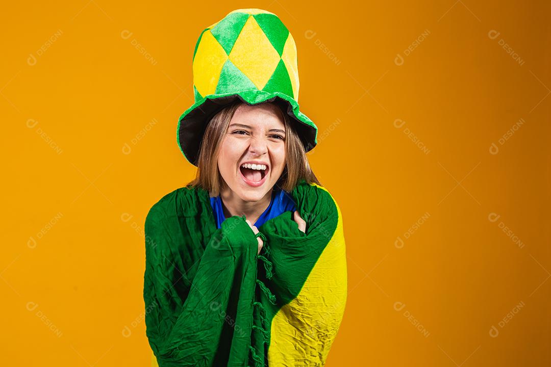 fã brasileira loira comemorando em fundo amarelo com bandeira do brasil