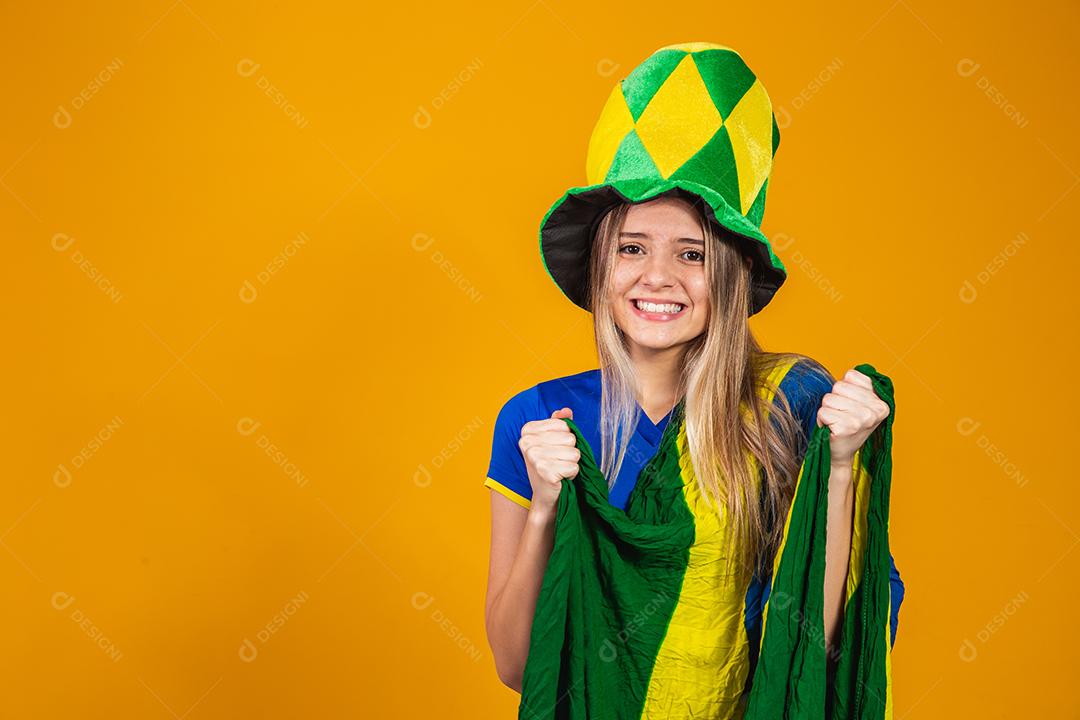 fã brasileira loira comemorando em fundo amarelo com bandeira do brasil