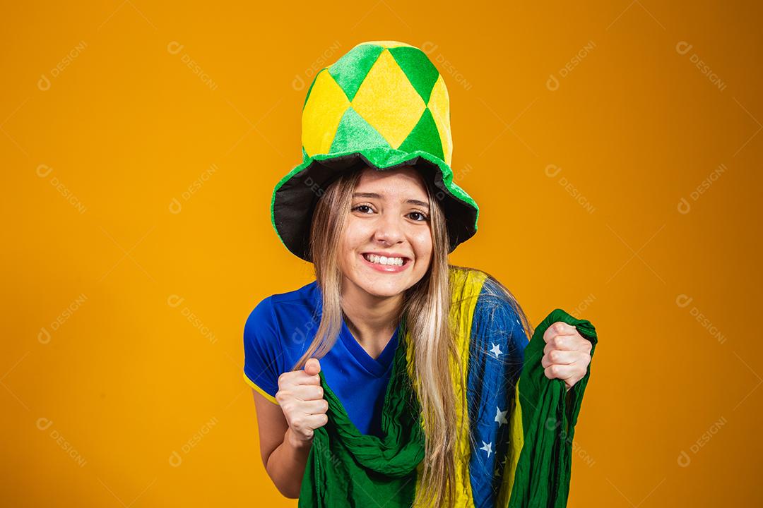 fã brasileira loira comemorando em fundo amarelo com bandeira do brasil
