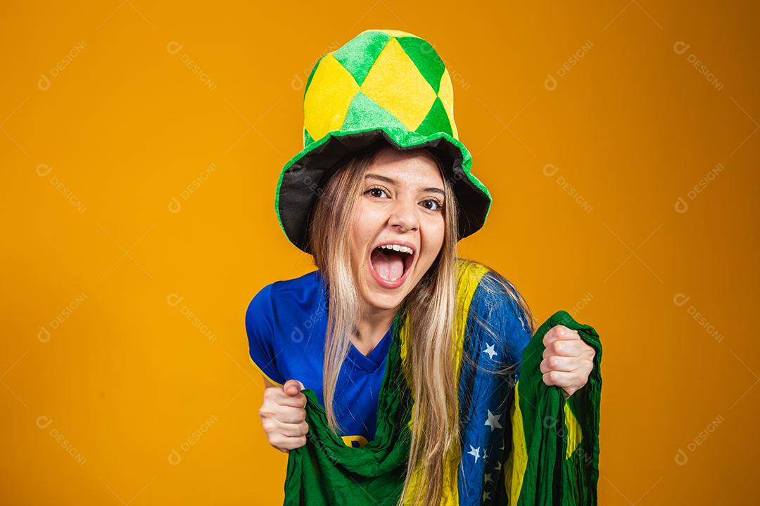 fã brasileira loira comemorando em fundo amarelo com bandeira do brasil