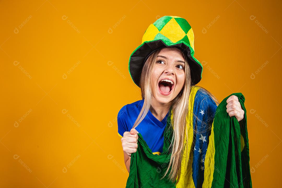 fã brasileira loira comemorando em fundo amarelo com bandeira do brasil