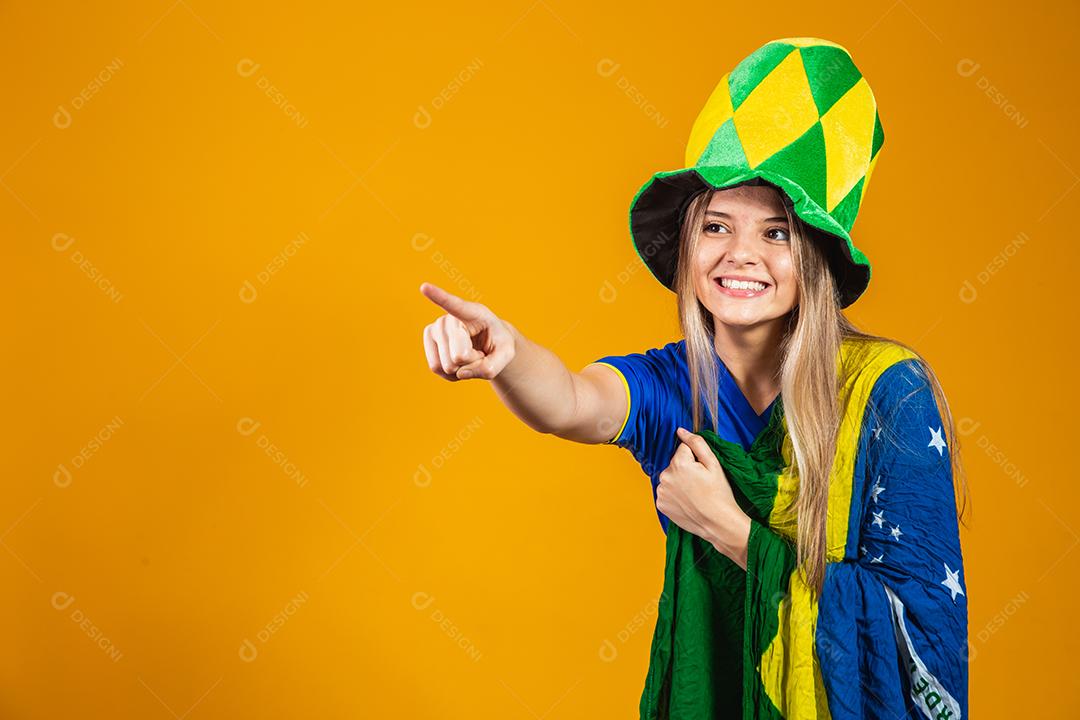 fã brasileira loira comemorando em fundo amarelo com bandeira do brasil