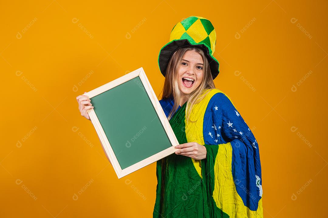 Mulher segurando Quadro Torcedora do brasil com chapéu e bandeira e expressão de felicidade em fundo amarelo