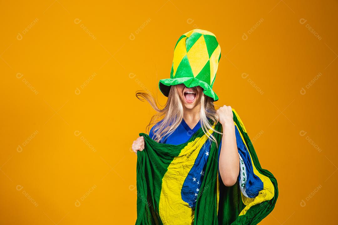 Mulher Torcedora do brasil com chapéu e bandeira e expressão de felicidade em fundo amarelo