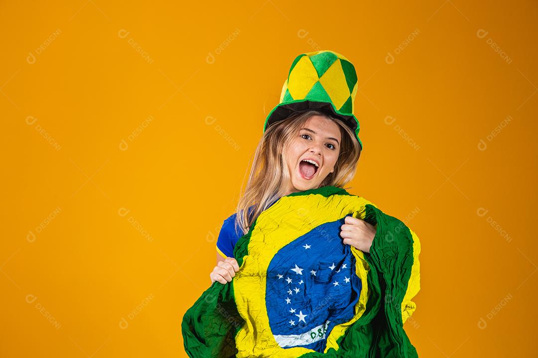 Mulher Torcedora do brasil com chapéu e bandeira e expressão de felicidade em fundo amarelo