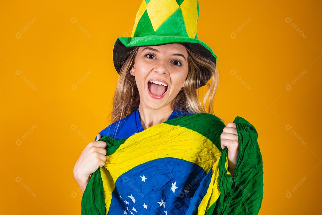 Mulher Torcedora do brasil com chapéu e bandeira e expressão de felicidade em fundo amarelo