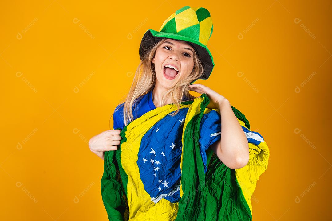 Mulher Torcedora do brasil com chapéu e bandeira e expressão de felicidade em fundo amarelo