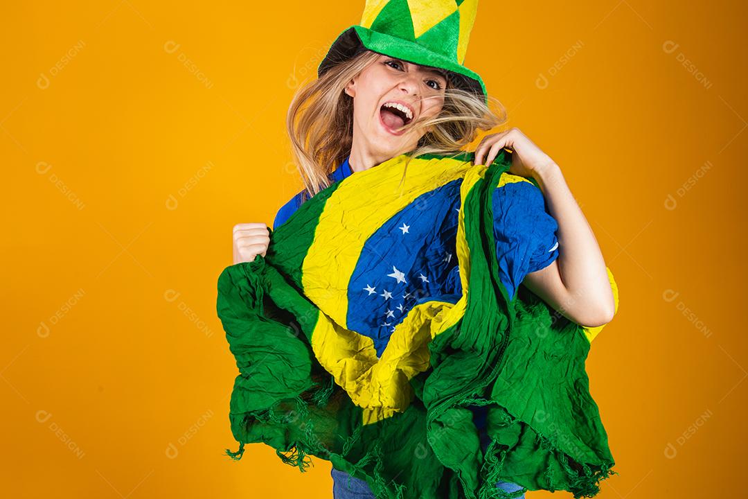Mulher Torcedora do brasil com chapéu e bandeira e expressão de felicidade em fundo amarelo