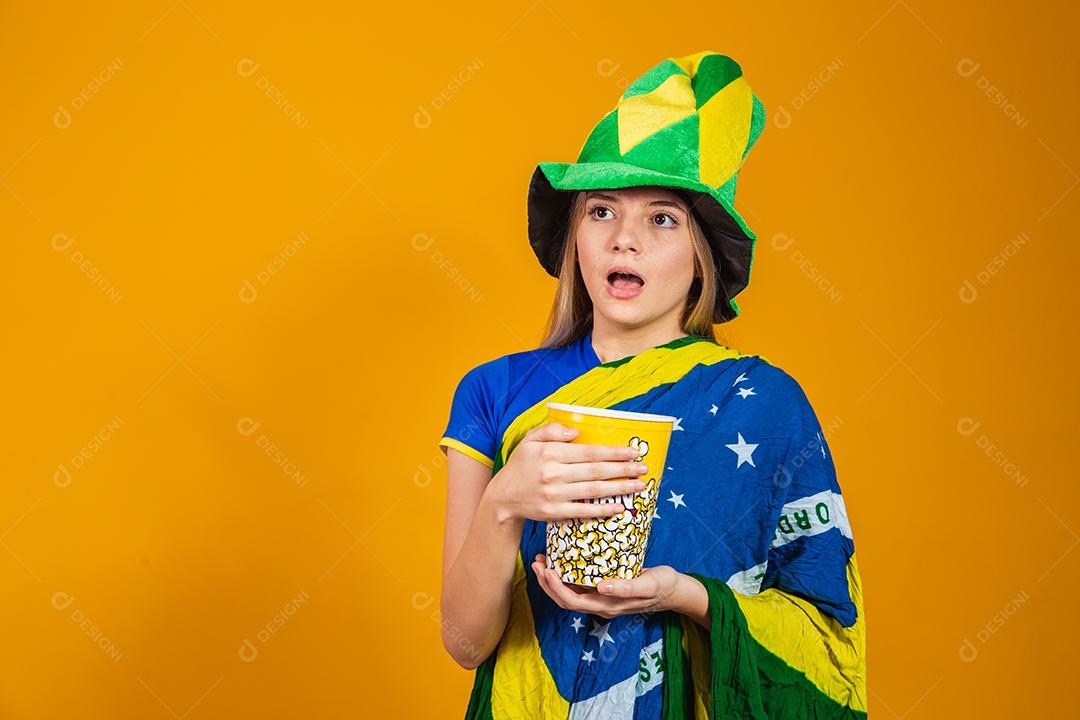 Mulher Torcedora do brasil com chapéu e bandeira segurando copo de pipoca em fundo amarelo