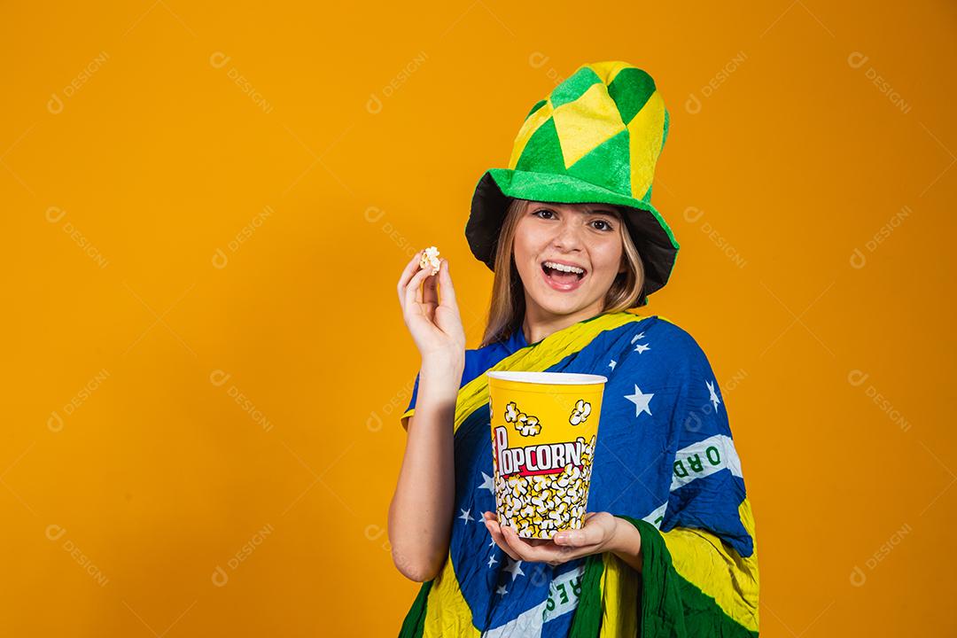 Mulher Torcedora do brasil com chapéu e bandeira segurando copo de pipoca em fundo amarelo
