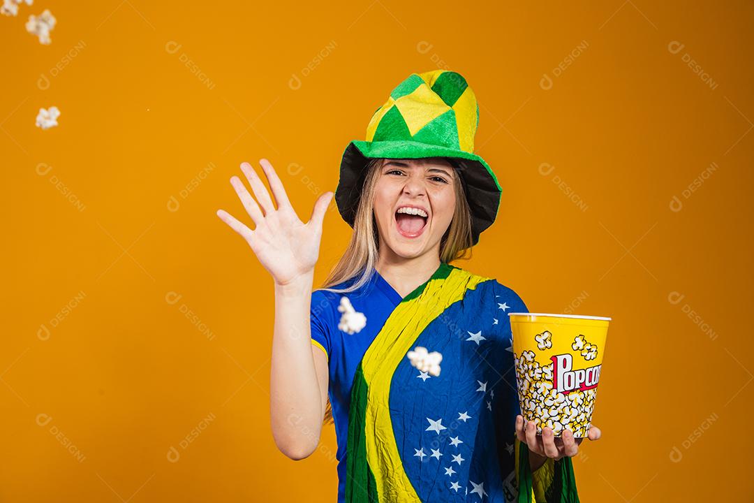 Mulher Torcedora do brasil com chapéu e bandeira segurando copo de pipoca em fundo amarelo