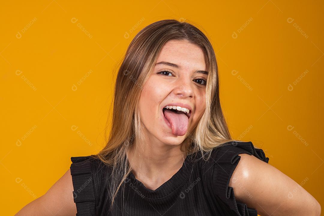 Mulher Com roupa preta e língua para fora feliz em fundo amarelo