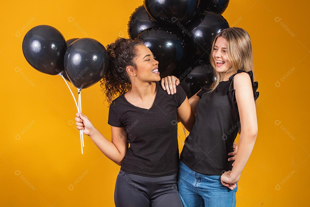 Duas namoradas em fundo amarelo com balões pretos na festa de promoção de sexta-feira negra.