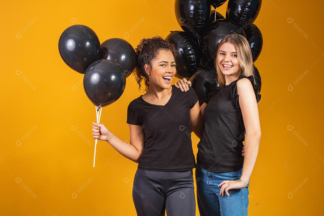 Duas namoradas em fundo amarelo com balões pretos na festa de promoção de sexta-feira negra.