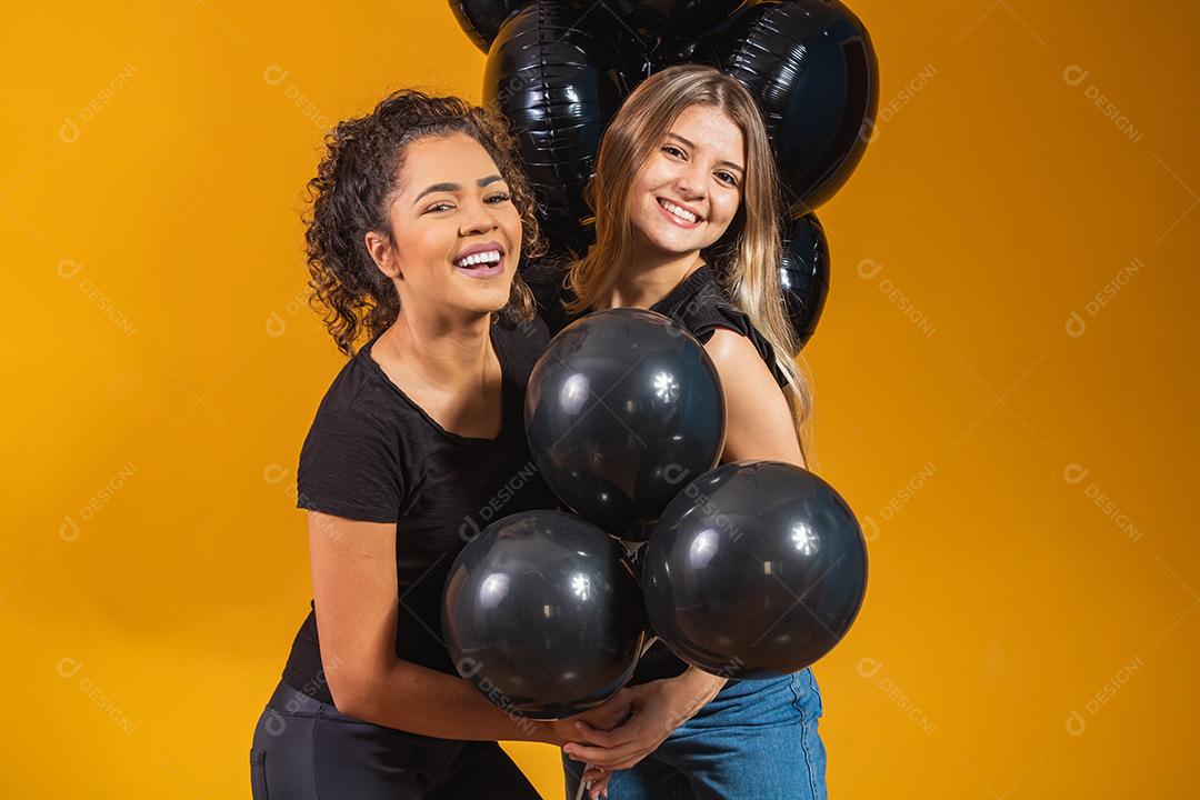 Duas namoradas em fundo amarelo com balões pretos na festa de promoção de sexta-feira negra.