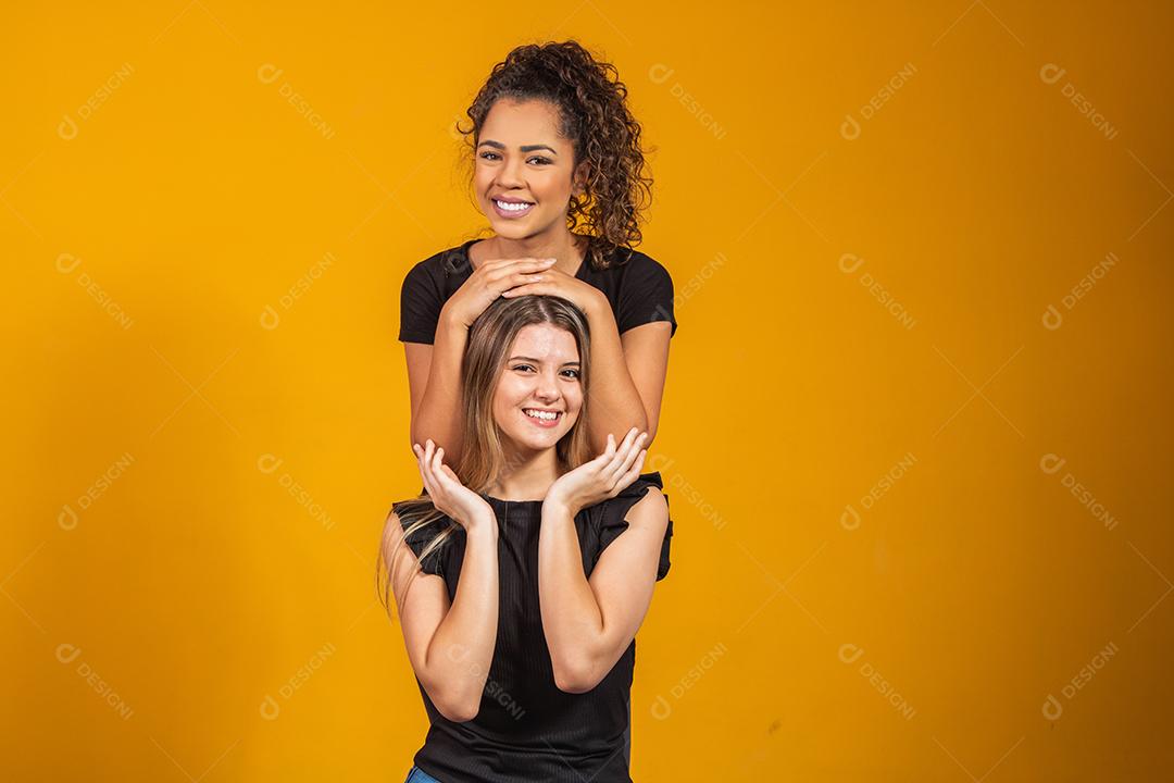amigas de diferentes etnias abraçados em fundo amarelo