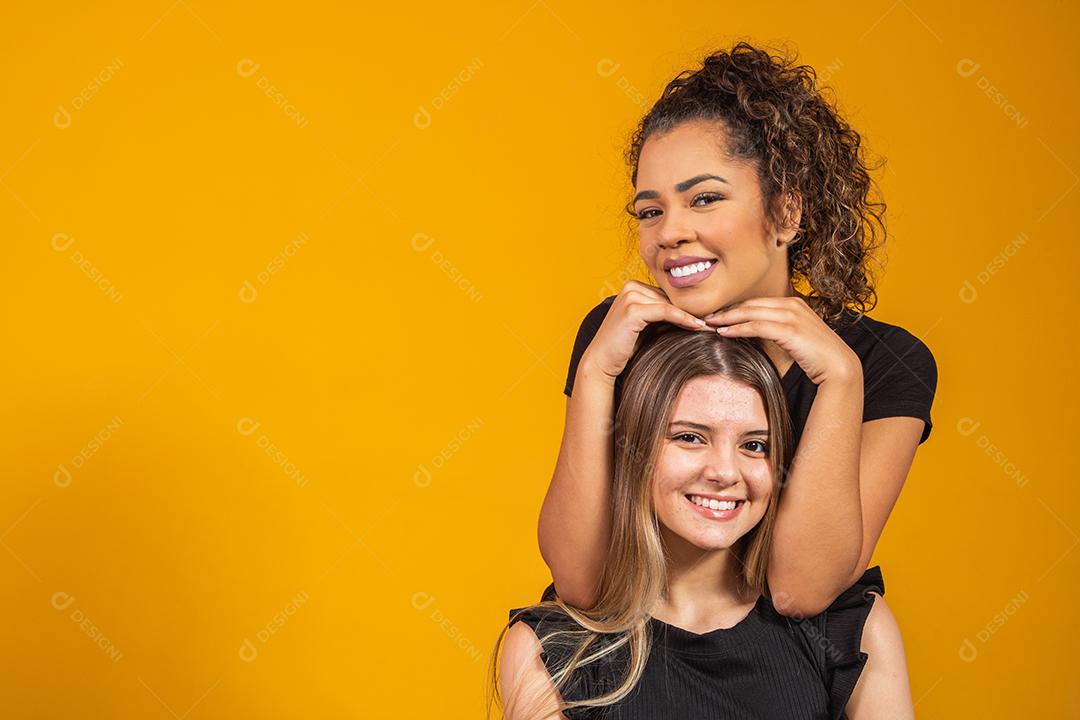 amigas de diferentes etnias abraçados em fundo amarelo