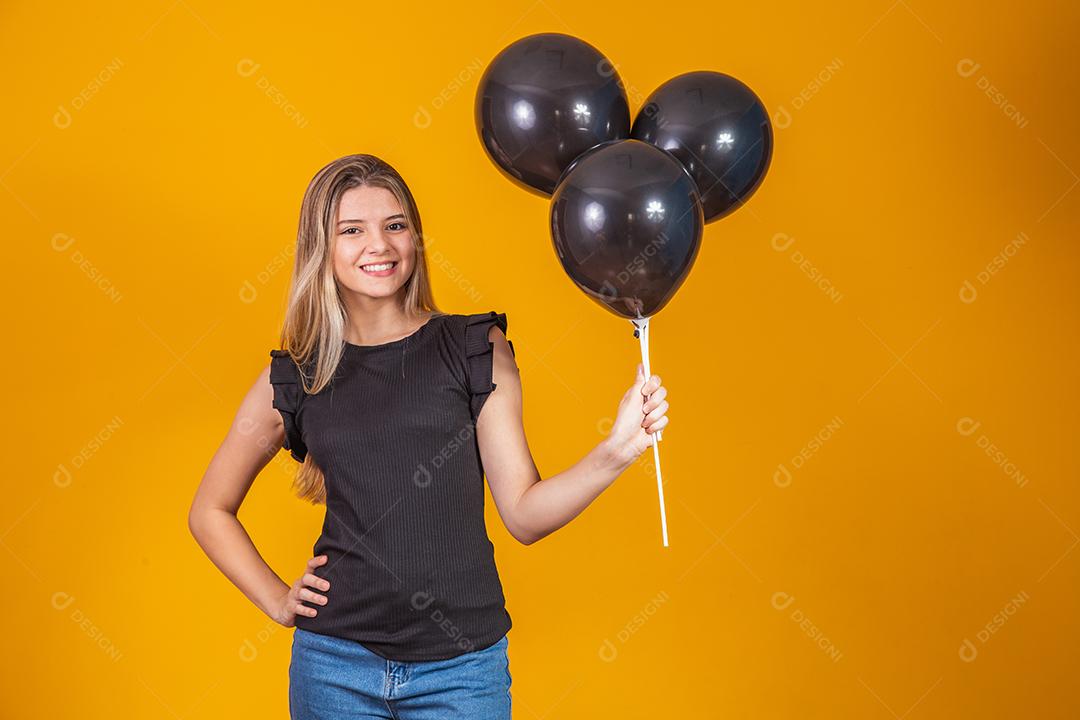 Mulher Com roupa preta segurando balões pretos em fundo amarelo