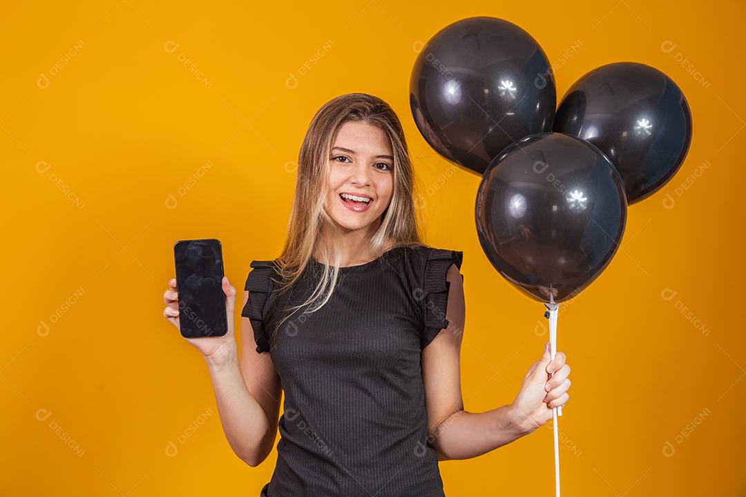 Sorrindo encantadora jovem segurando um celular com tela em branco vazia sobre fundo amarelo