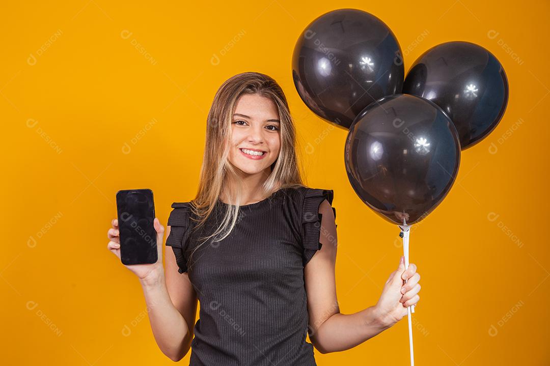 Sorrindo encantadora jovem segurando um celular com tela em branco vazia sobre fundo amarelo