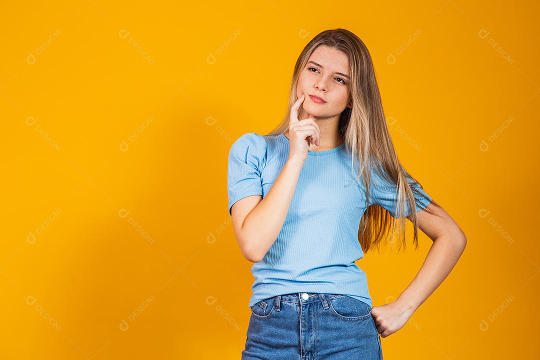 Mulher jovem pensativa em roupas casuais posando isolado no retrato de estúdio de fundo de parede amarela