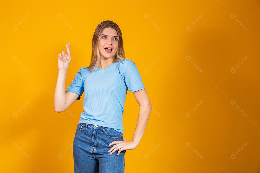 A imagem de uma jovem feliz e positiva isolada sobre o fundo da parede amarela faz um gesto esperançoso por favor