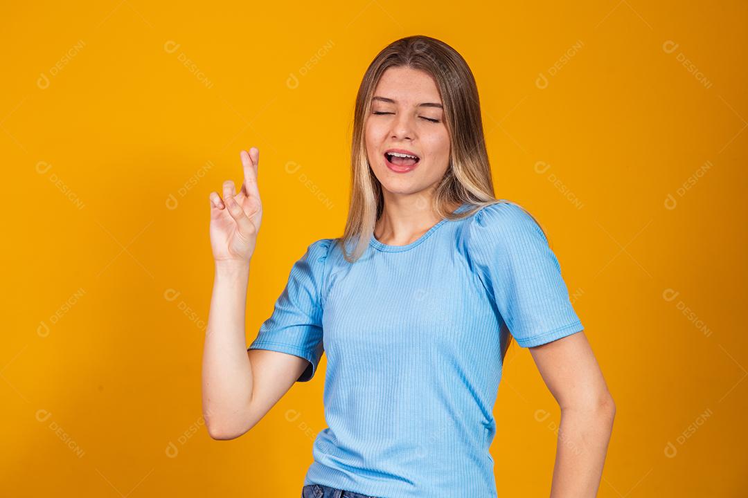 A imagem de uma jovem feliz e positiva isolada sobre o fundo da parede amarela faz um gesto esperançoso por favor