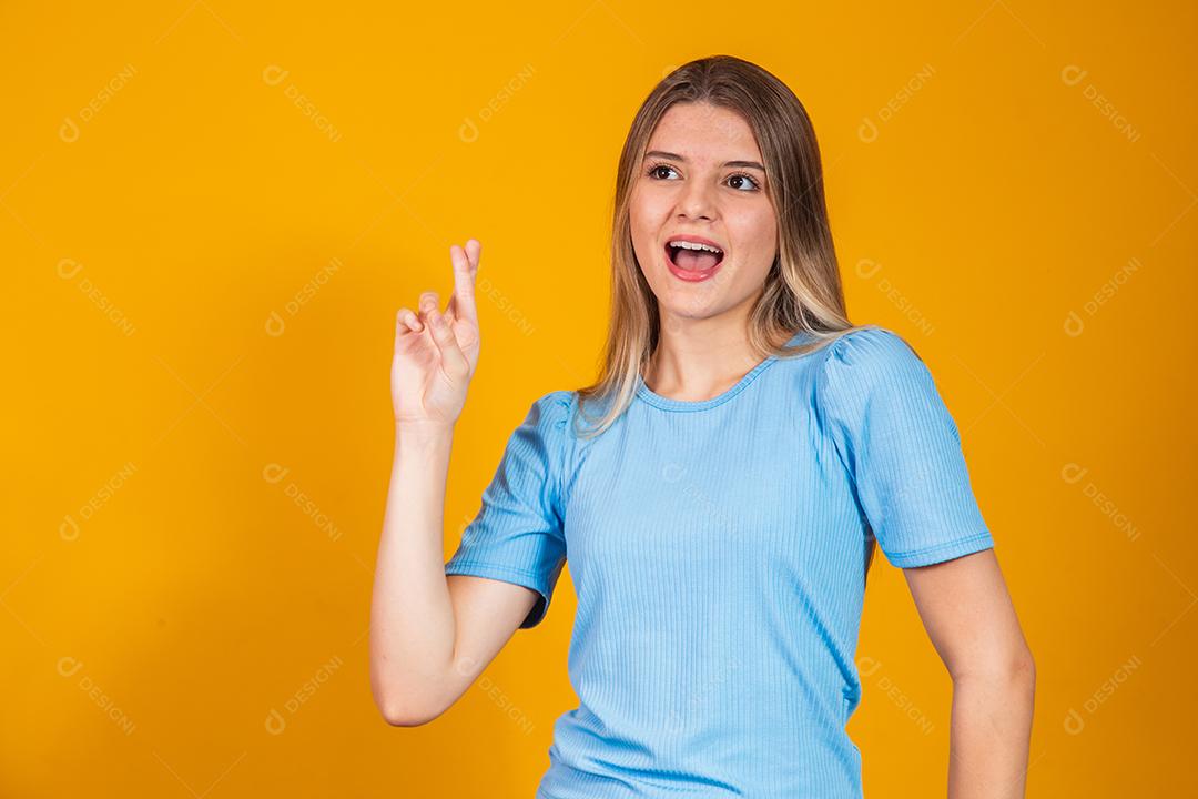 A imagem de uma jovem feliz e positiva isolada sobre o fundo da parede amarela faz um gesto esperançoso por favor