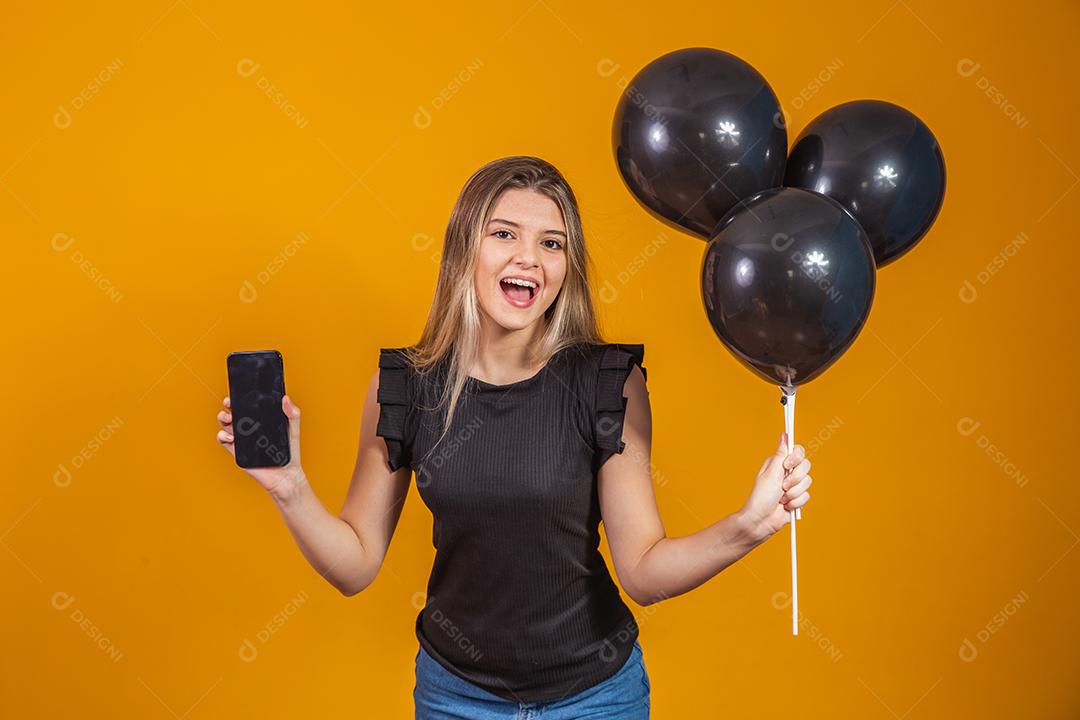 Sorrindo encantadora jovem segurando um celular e com Balões