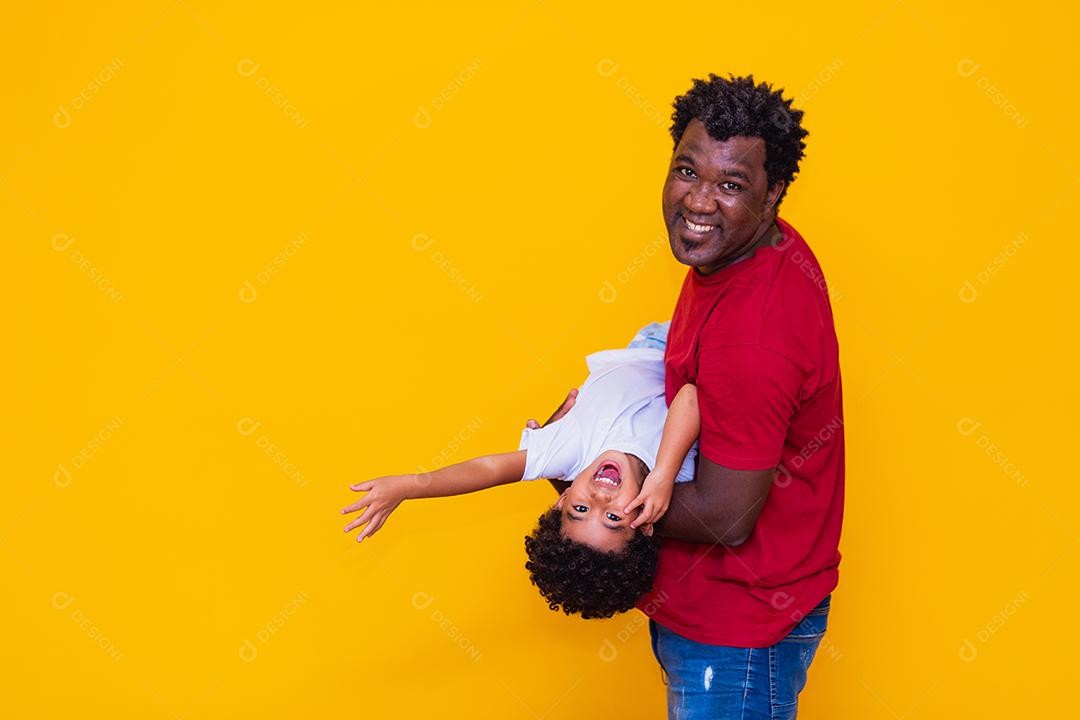 Pai e filho afro em fundo amarelo sorrindo e brincando