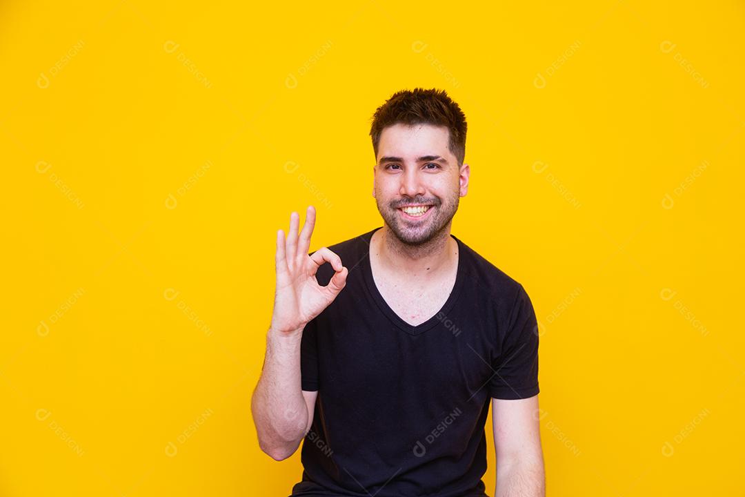 Retrato de um jovem alegre mostrando o gesto okey isolado em fundo amarelo