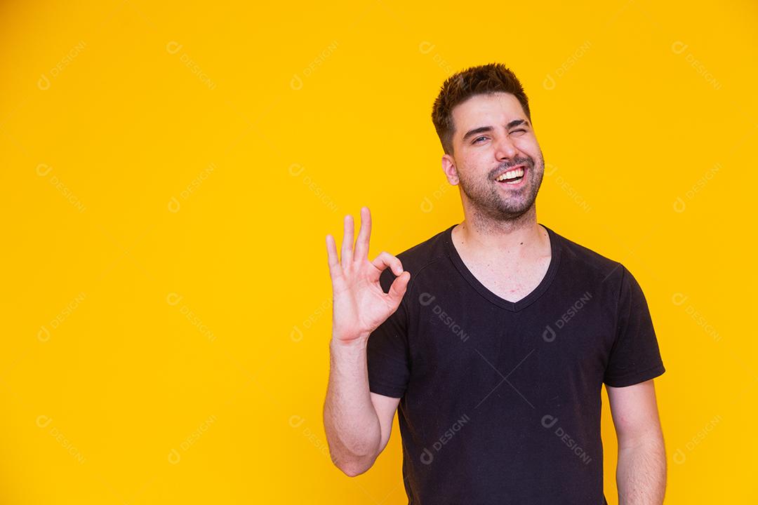 Retrato de um jovem alegre mostrando o gesto okey isolado em fundo amarelo