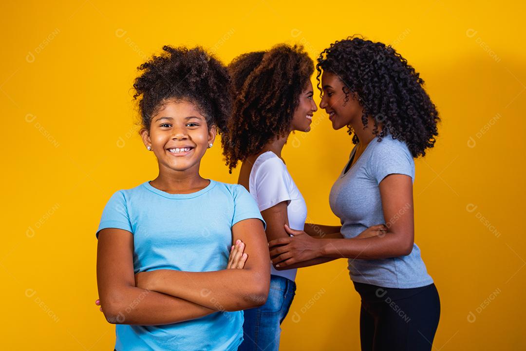 Feliz casal de lésbicas com criança em fundo amarelo. Casal junto com filha adotiva, conceito de adoção
