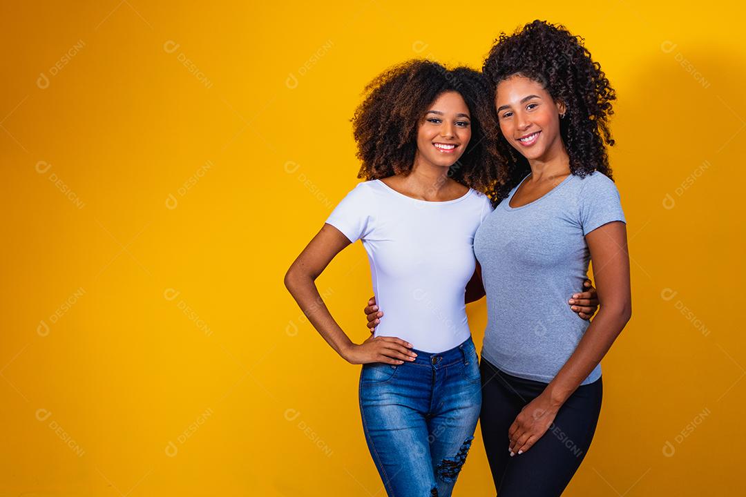 Lindas amigas afro com cabelos cacheados em fundo amarelo sorrindo.