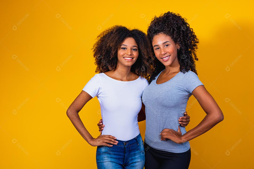 Lindas amigas afro com cabelos cacheados em fundo amarelo sorrindo.