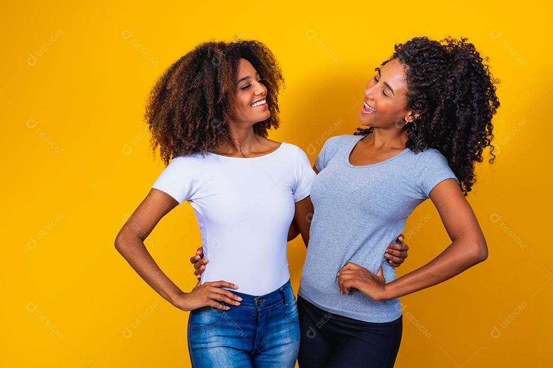 Lindas amigas afro com cabelos cacheados em fundo amarelo sorrindo.