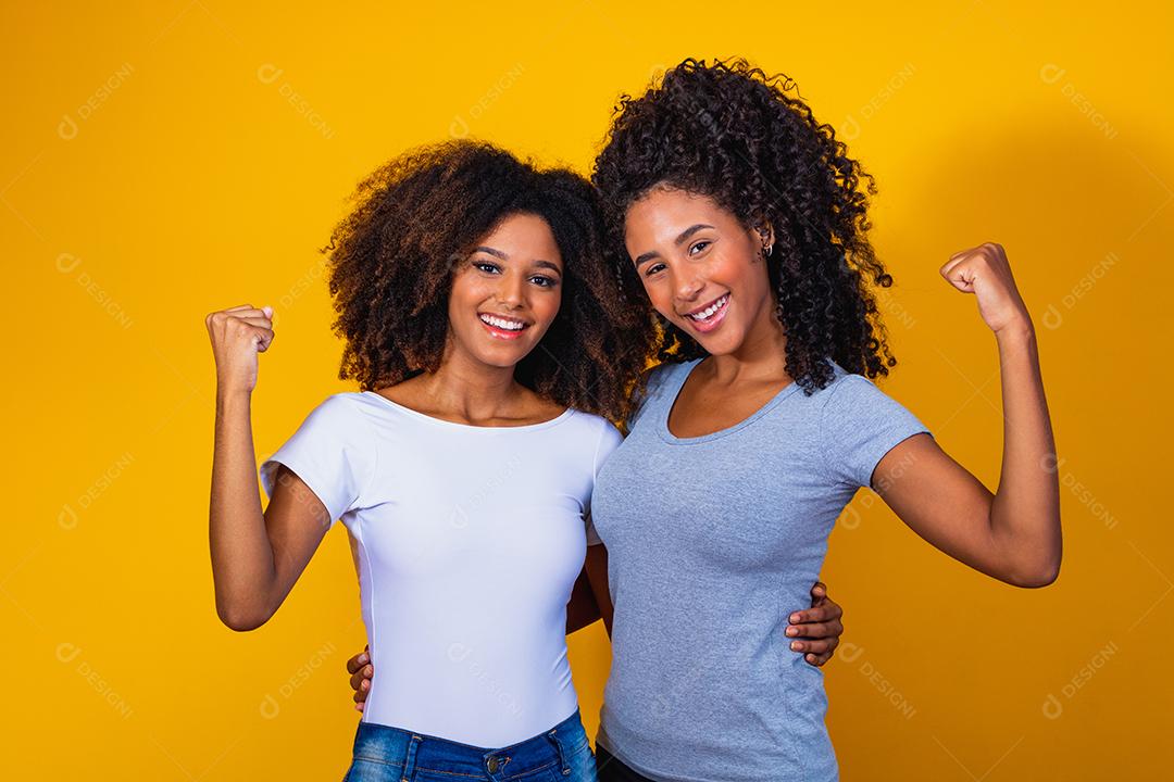 Lindas amigas afro com cabelos cacheados em fundo amarelo sorrindo.