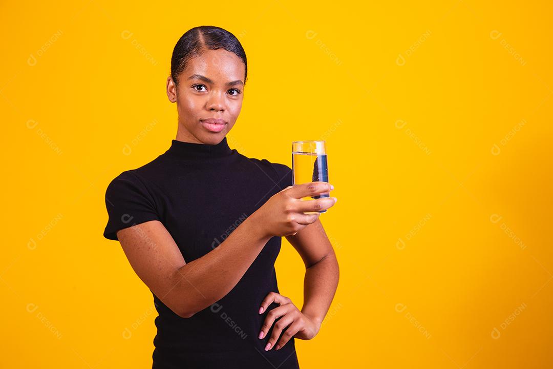 jovem afro bebendo água em fundo amarelo. Moça com copo de água