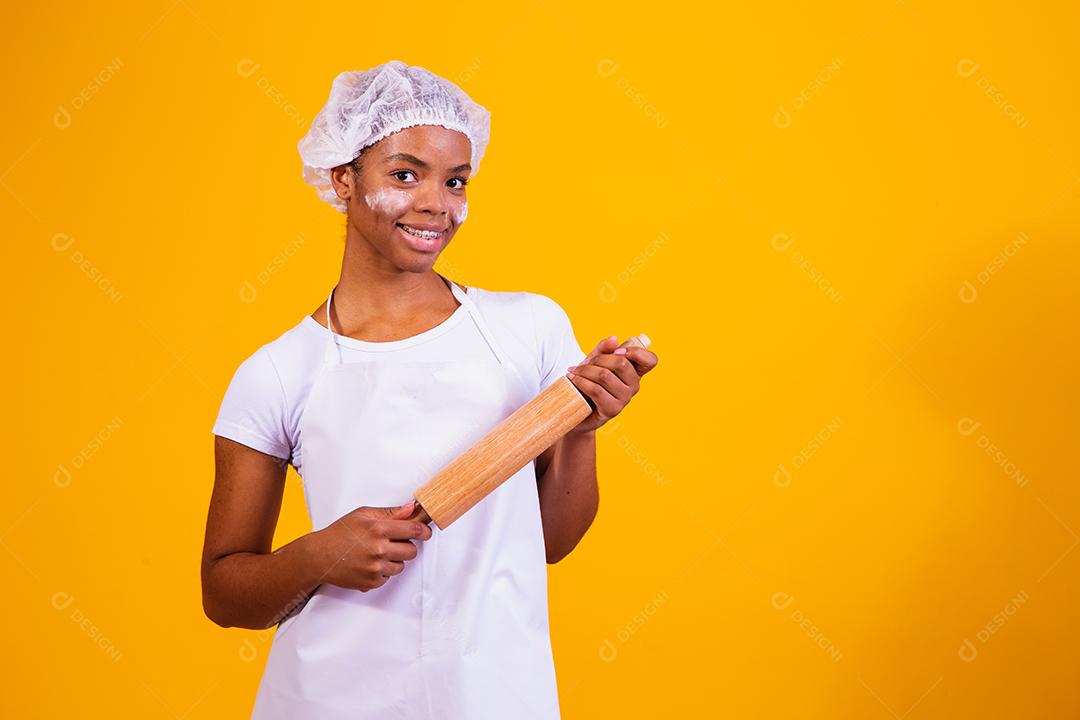 Mulher Com roupa de cozinheira e rolo de massa na mão em fundo amarelo
