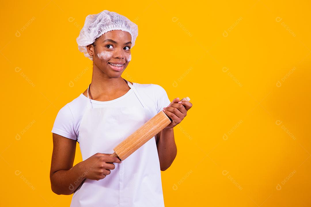 Mulher Com roupa de cozinheira e rolo de massa na mão em fundo amarelo