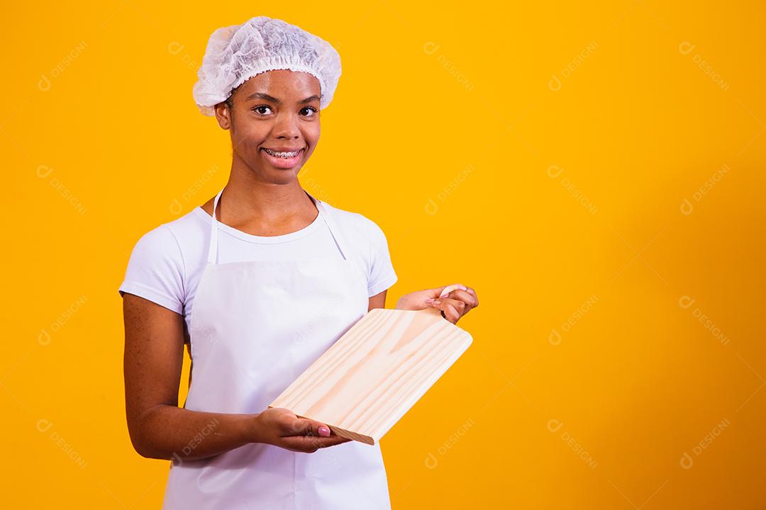 Mulher Com roupa de cozinheira e taboa de corte na mão em fundo amarelo