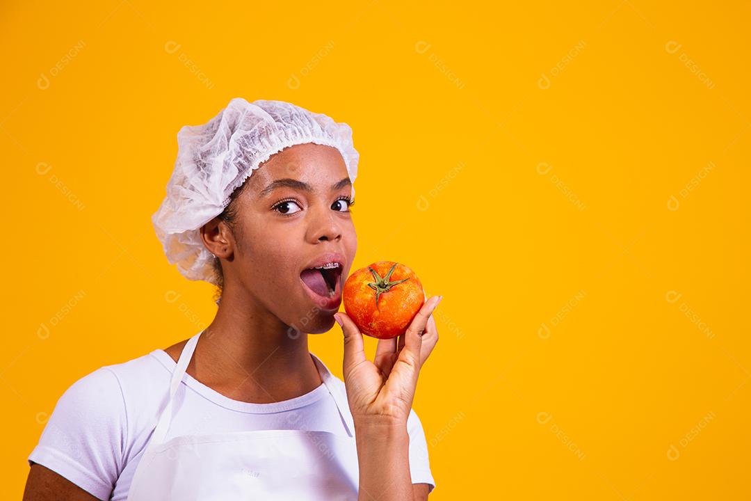 Mulher Com roupa de cozinheira com verdura na mão em fundo amarelo