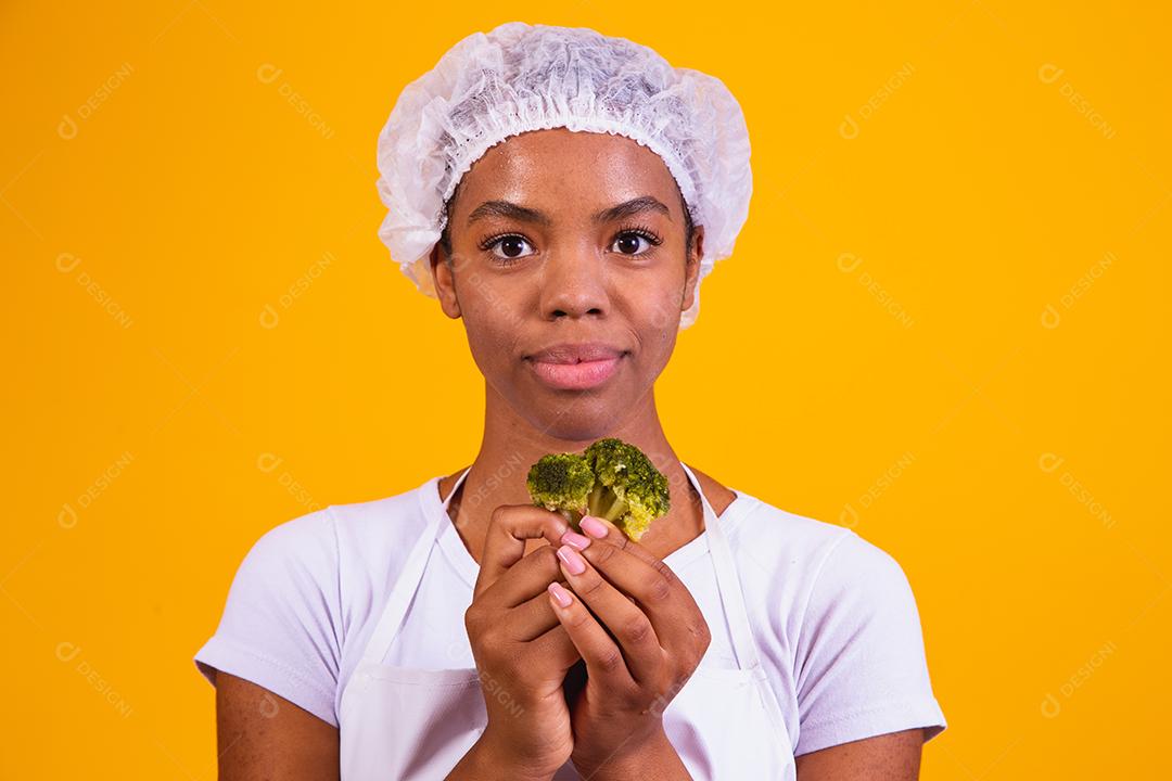 Mulher Com roupa de cozinheira com verdura na mão em fundo amarelo