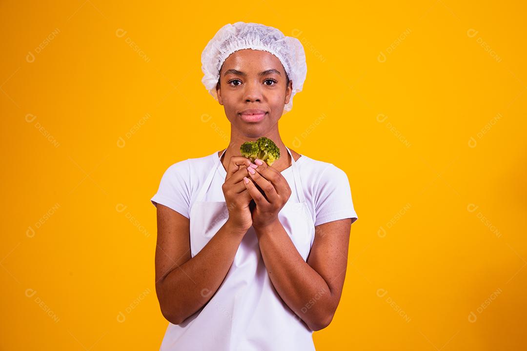 Mulher Com roupa de cozinheira com verdura na mão em fundo amarelo